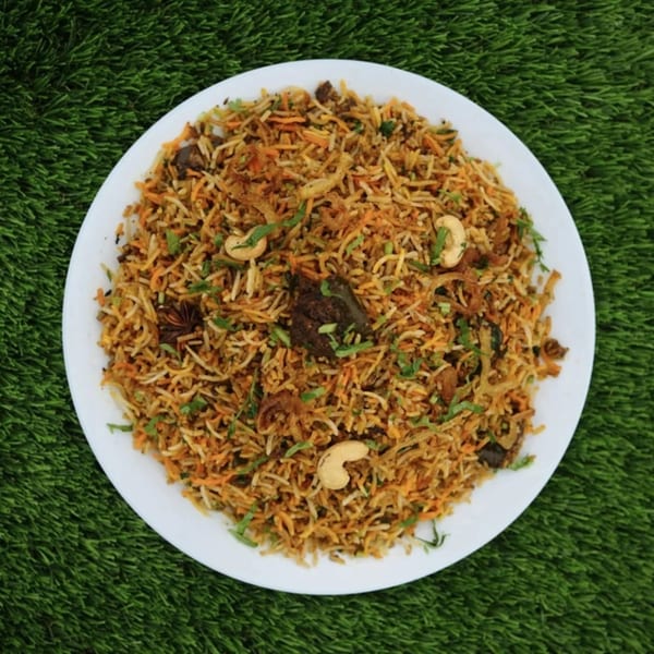 Little Spice Indian Cuisine's flavorful biryani with cashews and herbs on a white plate, against green turf.