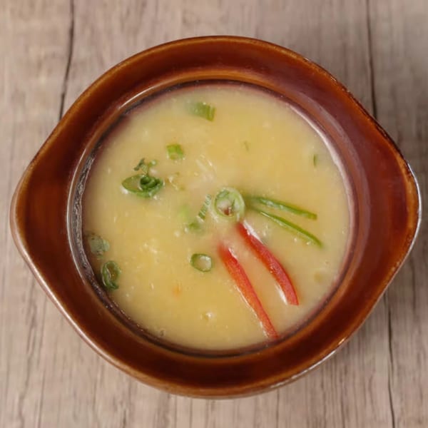Creamy yellow Indian soup in a brown bowl, garnished with green onions and red chili strips.