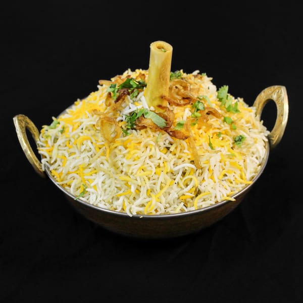 Little Spice Indian Cuisine's lamb shank biryani, garnished with fried onions and cilantro in a brass bowl.