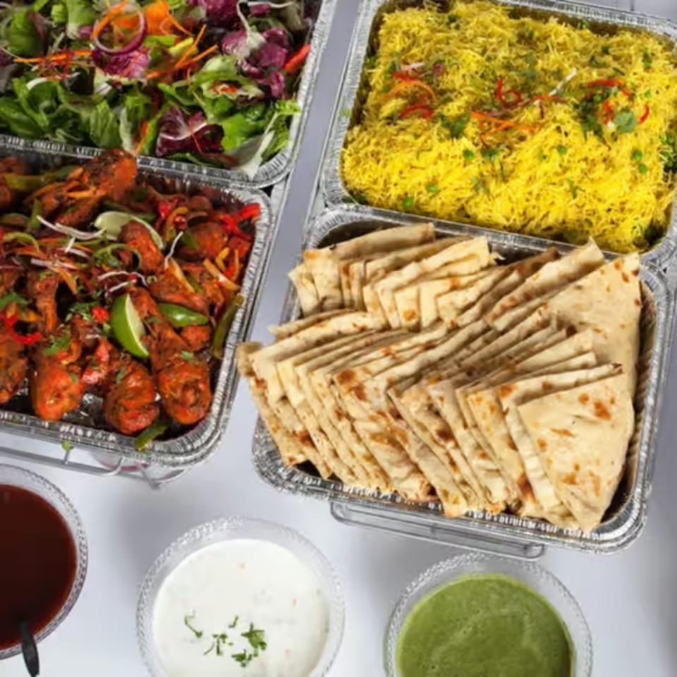 Indian catering spread with chicken, rice, salad, naan, and sauces in foil containers.