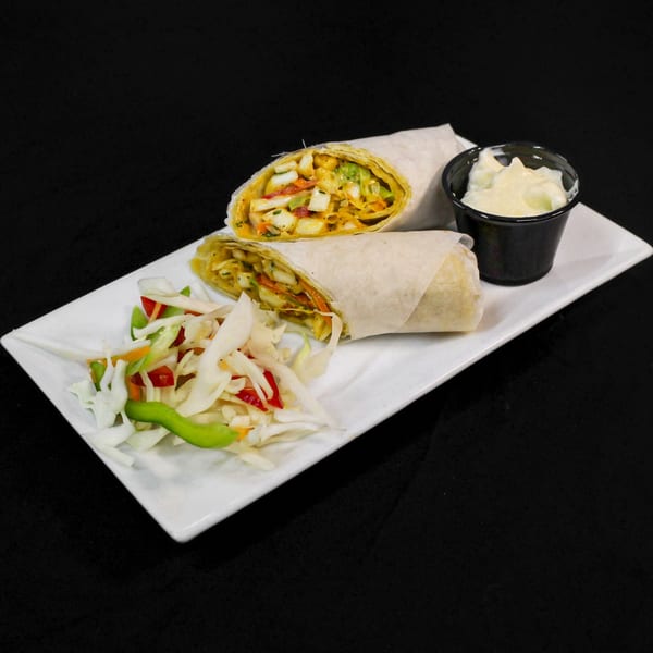 Two Indian wraps with colorful filling, a side salad, and a small cup of sauce on a white plate.