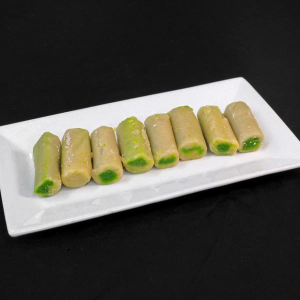 Eight Indian sweets, light brown with green centers, arranged on a white rectangular plate.