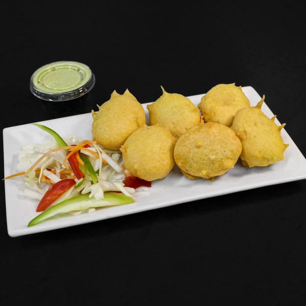 Six golden-fried Indian pakoras with a side of shredded salad and green chutney.