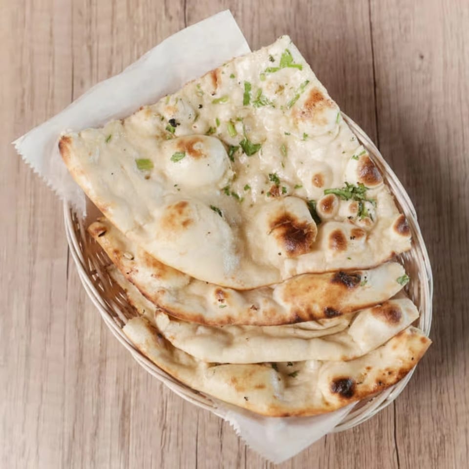Basket of warm, fluffy garlic naan bread with cilantro, served on a wooden table.