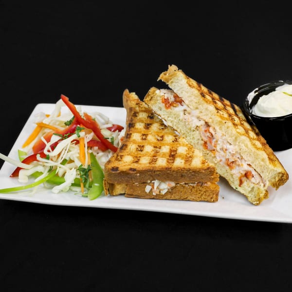 Grilled Indian sandwich with creamy filling, served with a side salad and white dipping sauce.