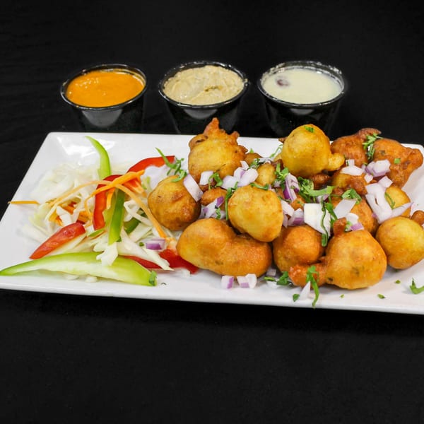 Golden-fried Indian pakora fritters with chopped onions, cilantro, a side salad, and three dipping sauces.