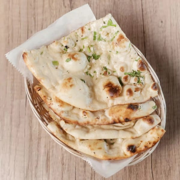 Basket of warm, fluffy garlic naan bread with cilantro, served on a wooden table.