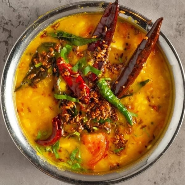 A close-up of Little Spice Indian Cuisine's yellow dal, garnished with red and green chilies, and spices.