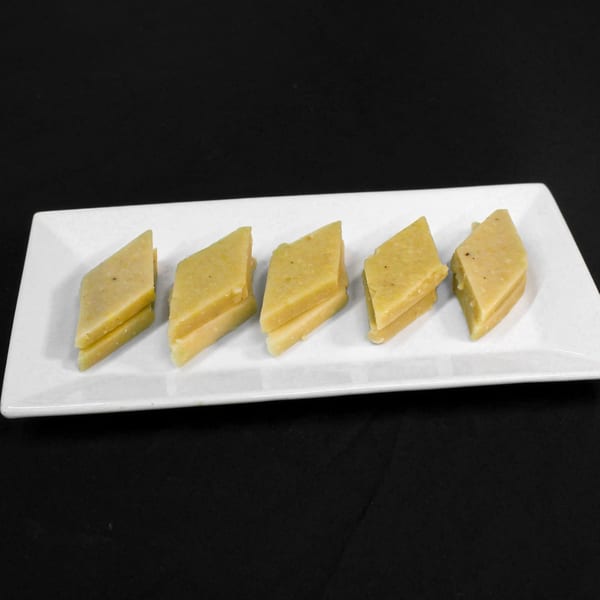 Five diamond-shaped pieces of light yellow Indian barfi dessert on a white rectangular plate.