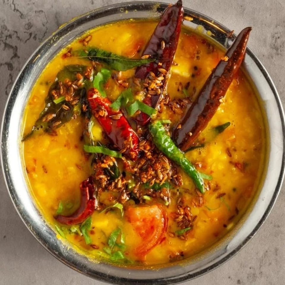 A close-up of Little Spice Indian Cuisine's yellow dal, garnished with red and green chilies, and spices.