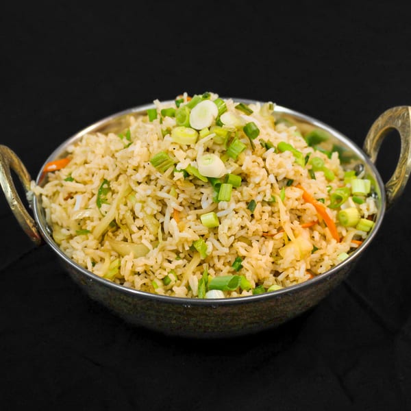 Indian fried rice with vegetables and green onions in a decorative metal bowl.