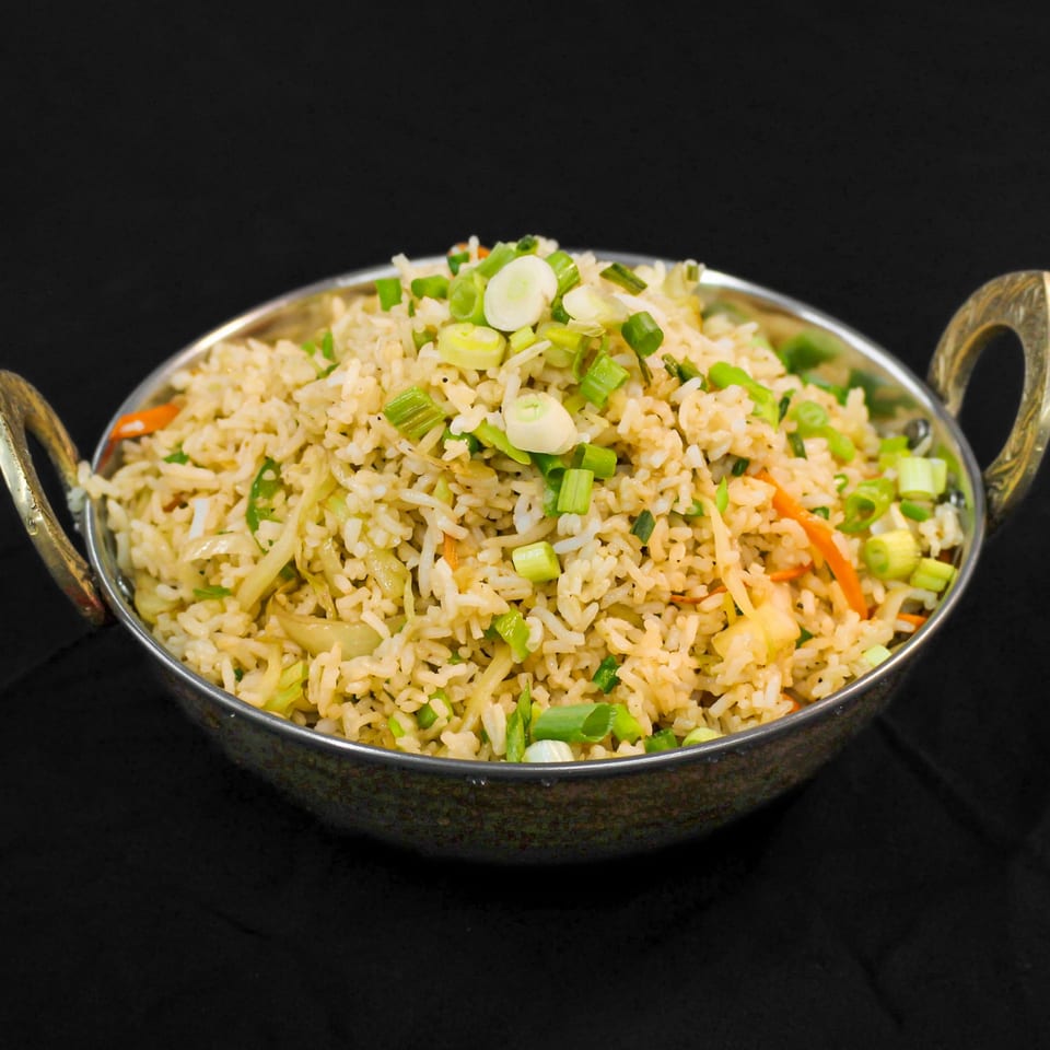Indian fried rice with vegetables and green onions in a decorative metal bowl.