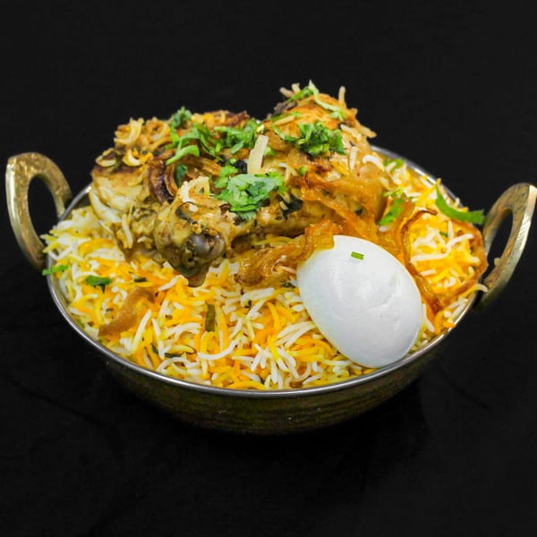 Chicken biryani with rice, fried onions, cilantro, and a boiled egg in a brass bowl.