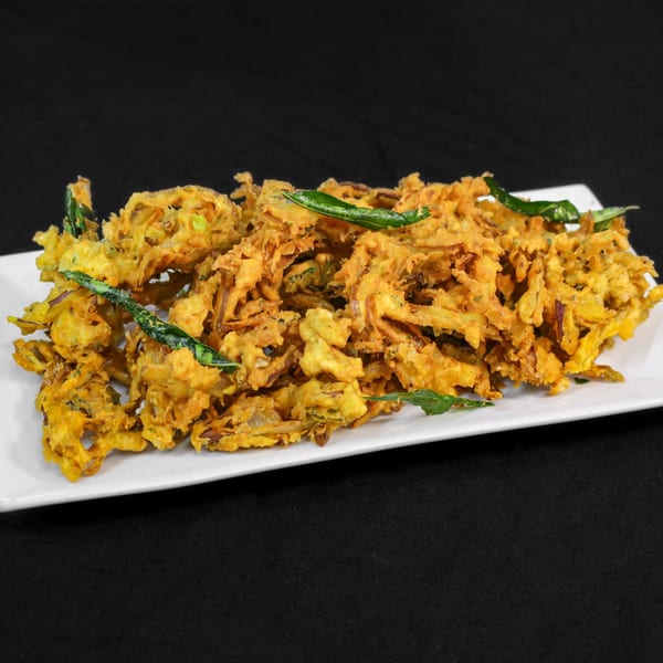 Crispy golden onion bhaji, an Indian appetizer, garnished with fresh green herbs on a white plate.